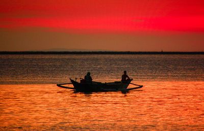Silhouette man in boat on sea against orange sky