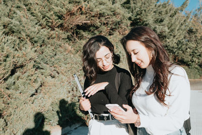 Smiling female friends using phone on sunny day