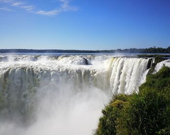 Scenic view of waterfall against blue sky