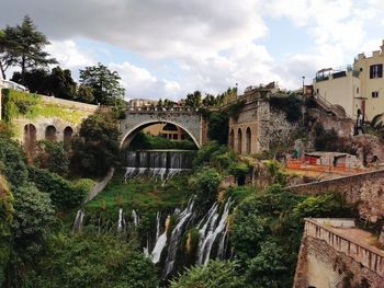 Arch bridge over river amidst buildings against sky