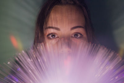 Close-up portrait of young woman holding illuminated fiber optic in darkroom