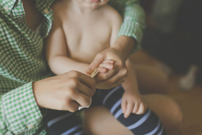 Midsection of mother cutting son's fingernail at home