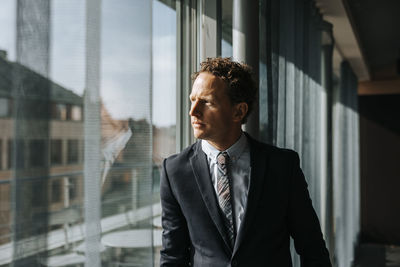 Mature male entrepreneur in suit looking through window at office