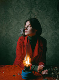 Side view of young woman holding illuminated lamp