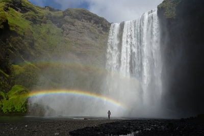 Person standing with double rainbow against skogafoss