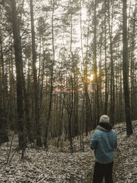 Rear view of man standing by trees in forest