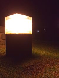 Illuminated lamp on field against sky at night