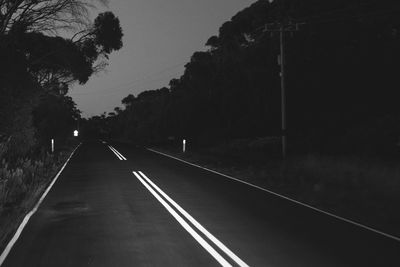 Empty road by trees against sky