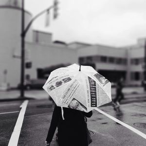 Rear view of person on street holding newspaper print umbrella during rains