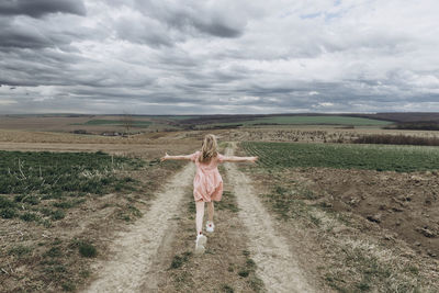 Carefree girl with arms outstretched running on pathway in agricultural field