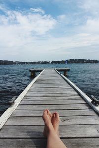 Low section of person on pier at lake against sky