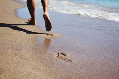 Low section of person walking on shore at beach during sunny day