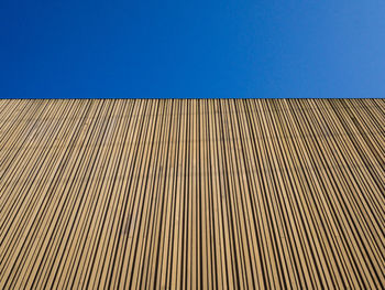 Low angle view of patterned wooden wall against clear blue sky