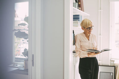 Woman standing reading book in home office