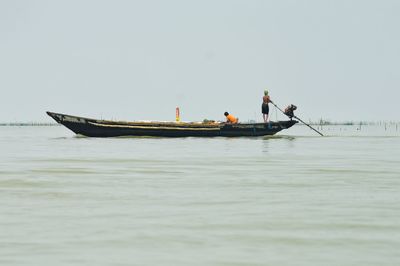 People on boat fishing in sea against clear sky