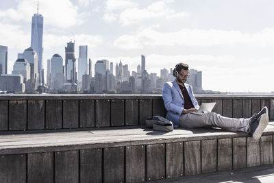 Usa, man wearing headphones using tablet at new jersey waterfront with view to manhattan