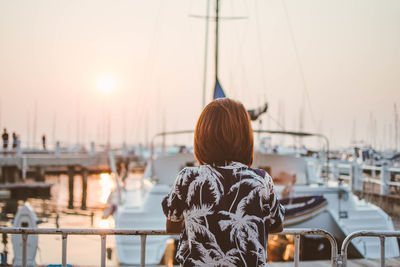 Rear view of woman standing at harbor against clear sky