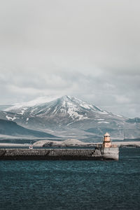 Scenic view of sea and snowcapped mountain against cloudy sky