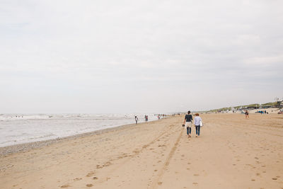 Rear view of female friends walking at beach against sky