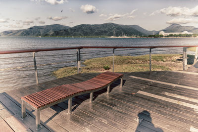 Empty bench by sea against sky