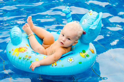 Portrait of shirtless girl sitting in inflatable ring on swimming pool