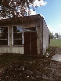 Abandoned building by trees on field against sky