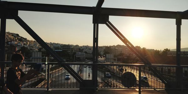 People on bridge in city against sky during sunset
