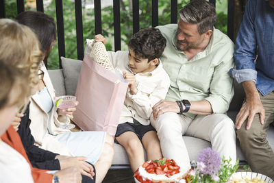 Surprised boy opening gift with family in patio