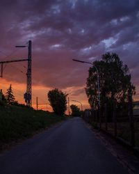 Road by silhouette trees against sky at sunset