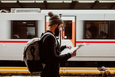 Side view of man reading map while standing at railroad station
