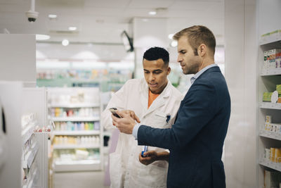 Mature customer showing mobile phone to male pharmacist standing at medical store