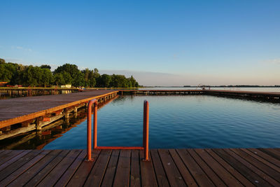 Scenic view of swimming pool by lake against clear blue sky