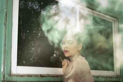 Portrait of young woman looking through window