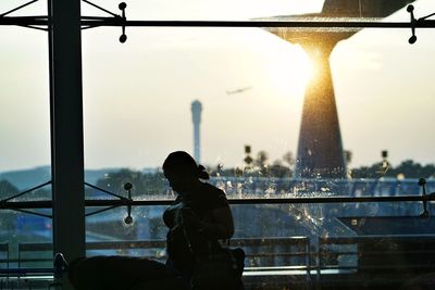 Rear view of silhouette man sitting by railing against sky