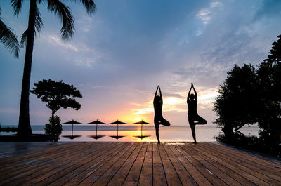 Silhouette people by swimming pool against sky during sunset