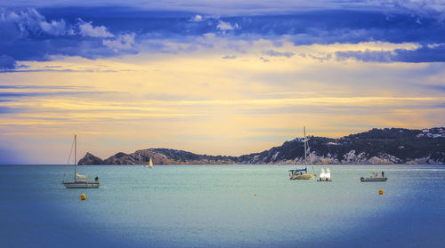 Sailboats sailing in sea against sky during sunset