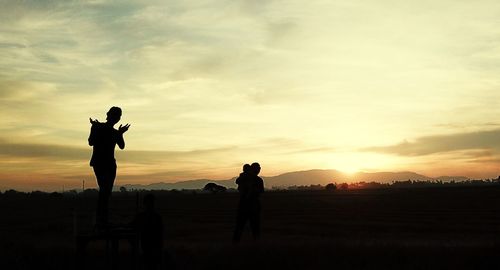 Silhouette people standing on field against sky during sunset