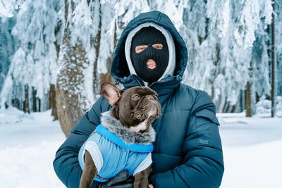 Man with ski mask and french bulldog in winter forest