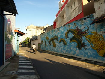 Rear view of man riding motorcycle on street amidst graffiti wall