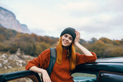 Portrait of a smiling young woman sitting on car
