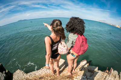 Rear view of women standing by sea against sky