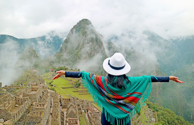 Woman in blue poncho being impressed by the amazing ancient inca citadel of machu picchu, peru