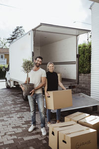 Portrait of smiling male and female partners unloading cardboard boxes during relocation