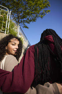 Low angle portrait of smiling young woman with arm around female friend