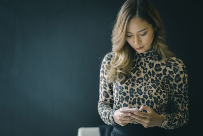 Young woman looking away while standing against black background