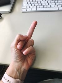 Cropped hand of person showing obscene gesture by keyboard on table