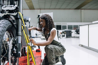 Side view of african american female mechanic with wrench fixing custom motorbike while working in workshop