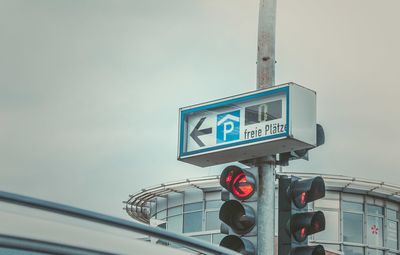 Low angle view of road sign and signal on pole against sky