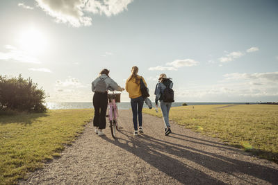 Rear view of female friends walking at lakeshore against sky