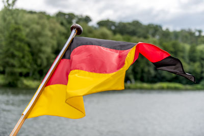 Flag of germany flutters in the colors black red gold at the stern of a boat over water in the wind